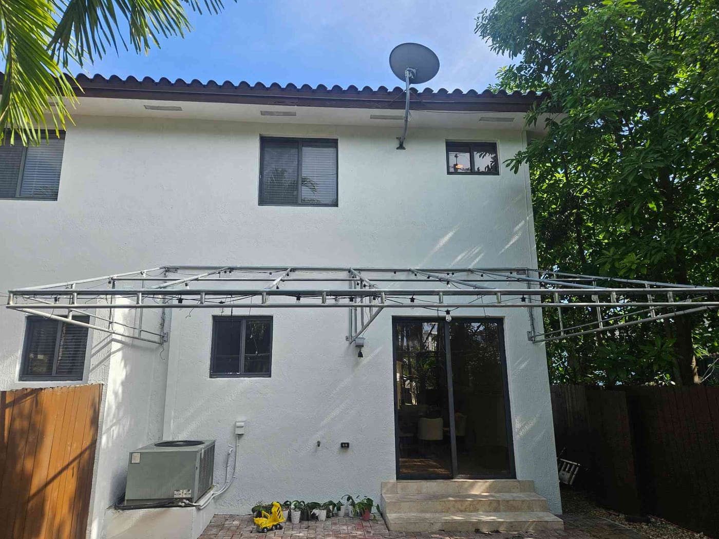 Freshly repainted white rear exterior of a two-story home with a satellite dish and pergola frame