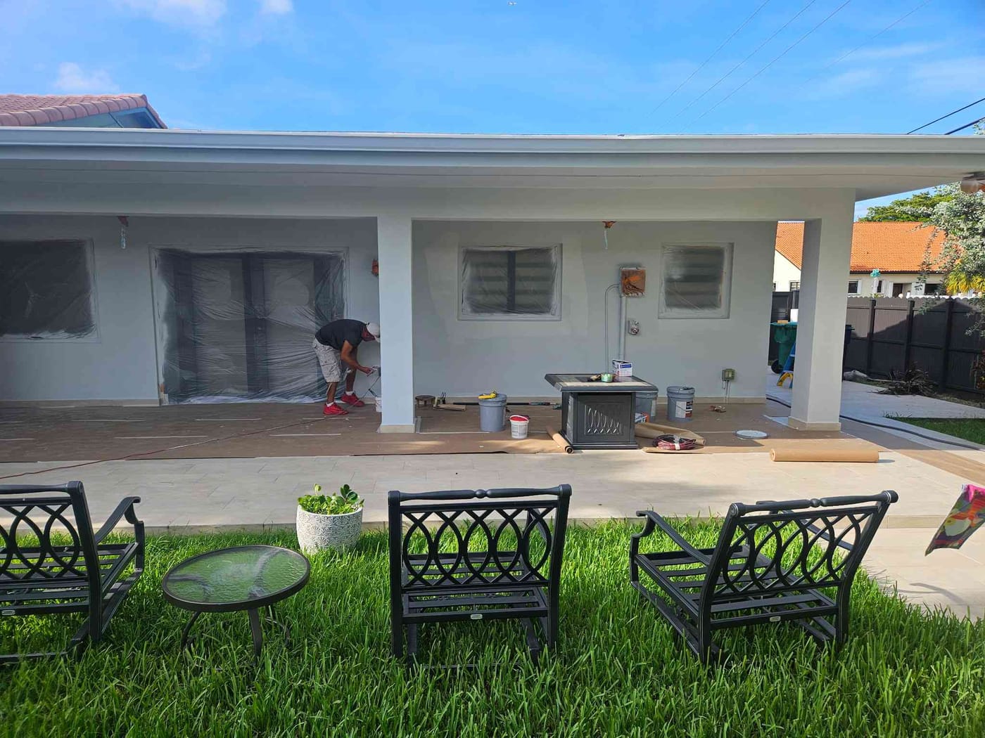 Painter masking windows on a white single-story home with a covered back patio overlooking the lawn