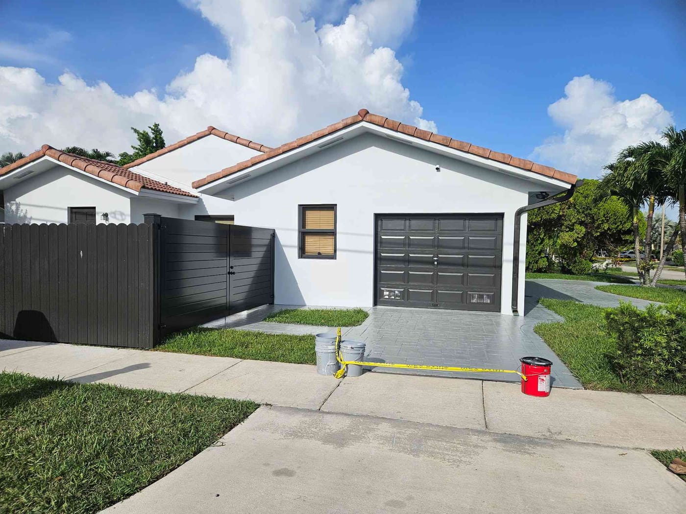 Single-story home with a freshly painted dark garage door and white stucco, wet-paint tape across the driveway