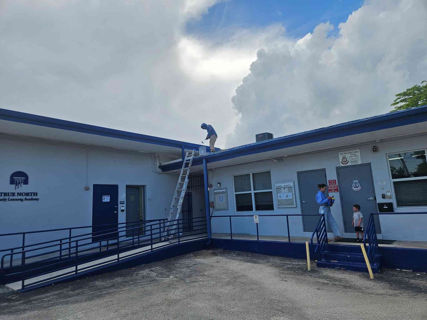Painter on the roof edge repainting a community learning-center building with crisp blue trim