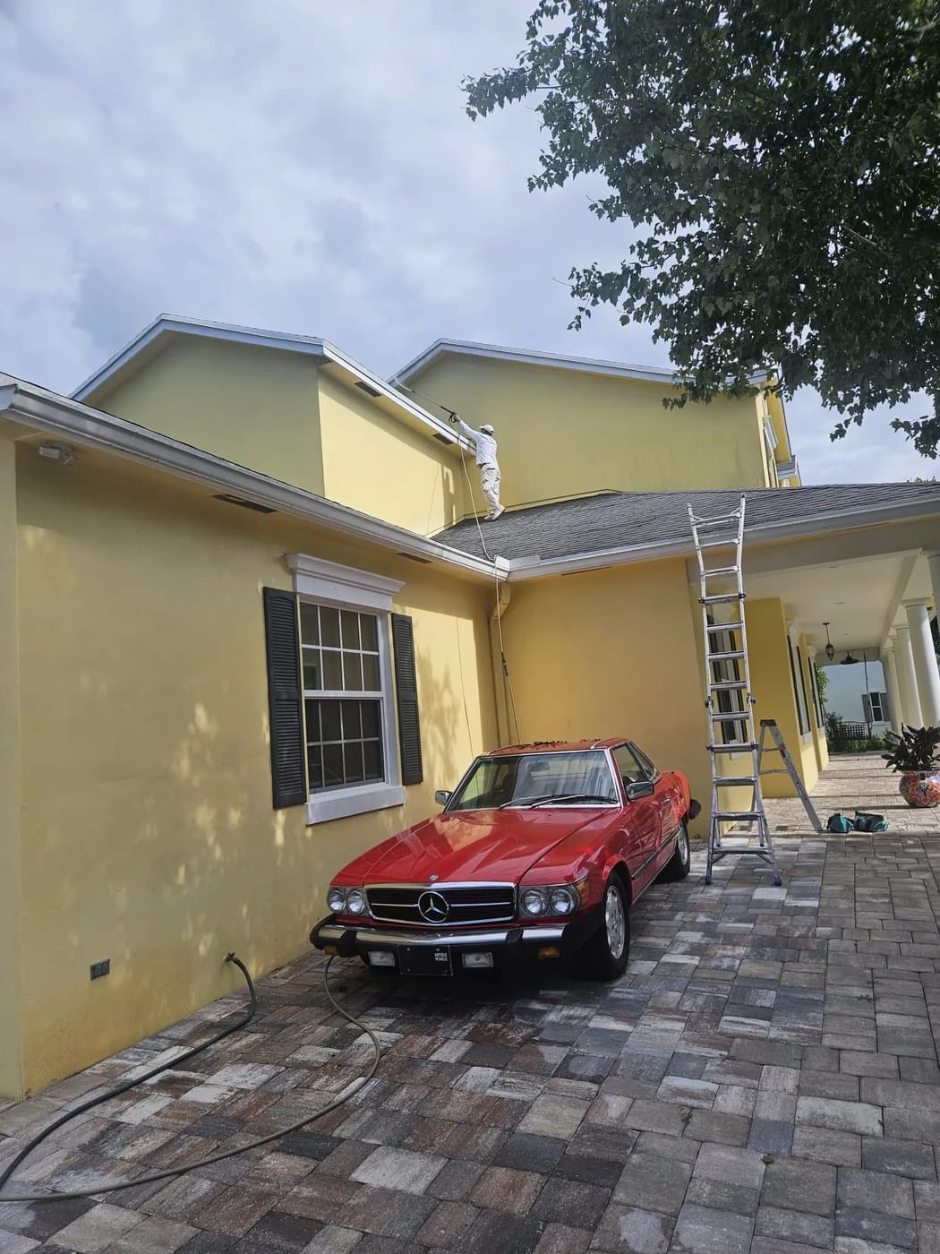 Residential painting — yellow two-story home with painter on ladder